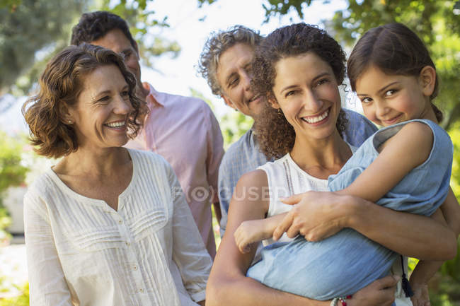 Mother carrying daughter in arms with family outdoors — Stock Photo