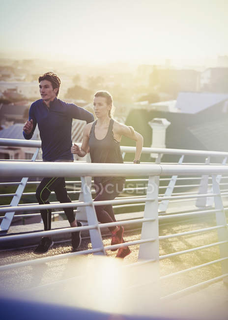 Runner couple running on sunny urban footbridge at sunrise — Stock Photo