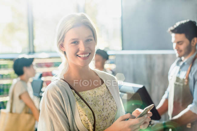 Портрет улыбающейся молодой женщины с сотовым телефоном на кассе продуктового магазина — стоковое фото