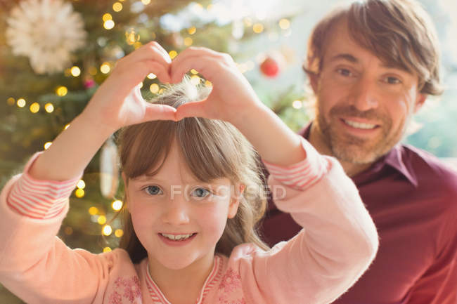 Portrait smiling father and daughter forming heart-shape near Christmas tree — Stock Photo