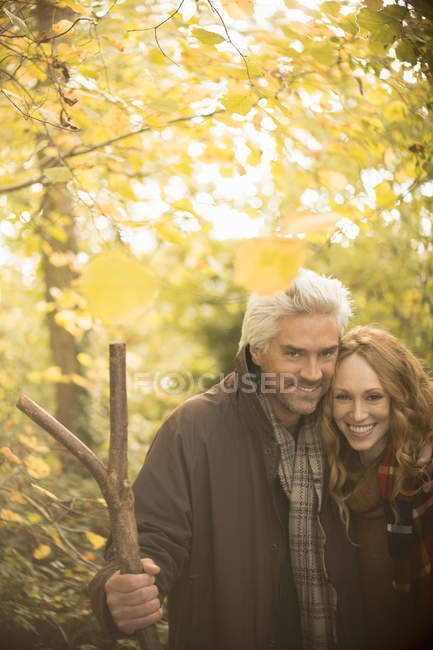 Retrato sonriente pareja con bastón en los bosques de otoño - foto de stock