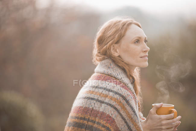 Serene woman wrapped in blanket drinking hot coffee outdoors — Stock Photo