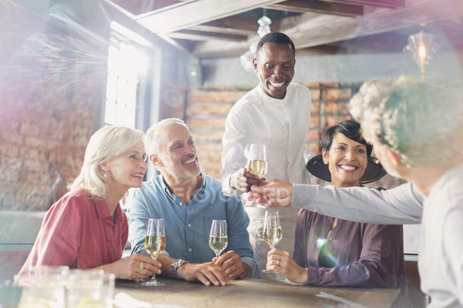 Camarero sirviendo vino blanco a parejas en mesa de restaurante - foto de stock