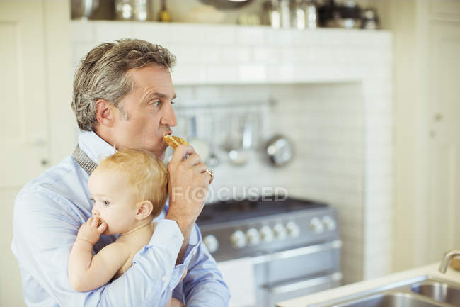 Father holding baby and eating breakfast — Stock Photo