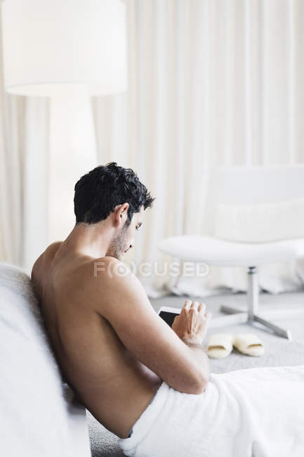 Man in towel using digital tablet in bedroom at home — Stock Photo