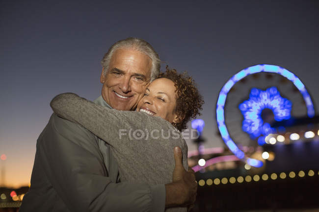 Portrait of couple hugging outside amusement park at night — Stock Photo