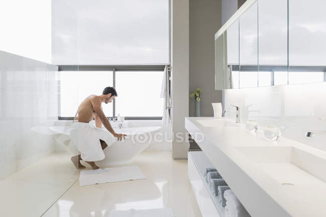 Hombre guapo en toalla preparando baño en casa - foto de stock