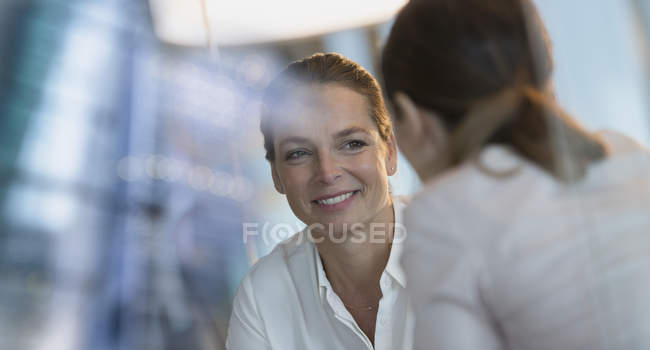 Mujer de negocios sonriente escuchando a su colega, fondo borroso - foto de stock
