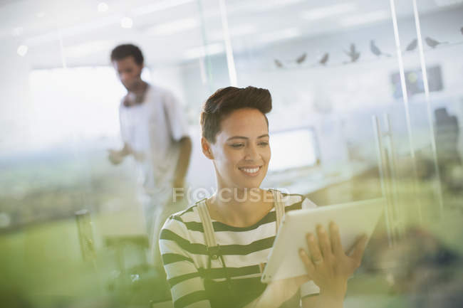 Улыбающаяся креативная деловая женщина с помощью цифрового планшета в офисе — стоковое фото