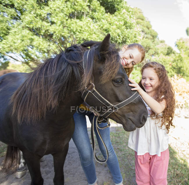 Mother and daughter petting horse outdoors — Stock Photo