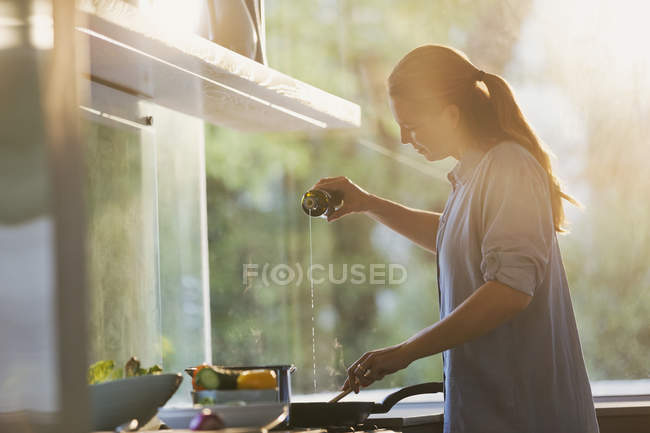 Woman pouring oil into pan on stove in kitchen — Stock Photo