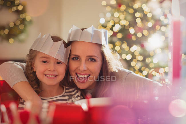 Portrait enthusiastic mother and daughter in paper crowns at Christmas dinner table — Stock Photo