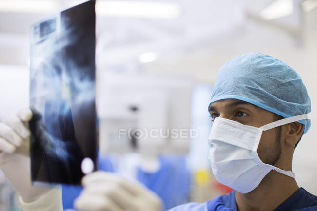 Primer plano del cirujano con gorra quirúrgica y máscara mirando rayos X en quirófano - foto de stock