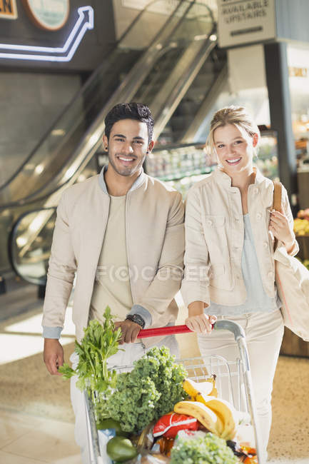 Portrait smiling young couple with shopping cart grocery shopping in market — Stock Photo