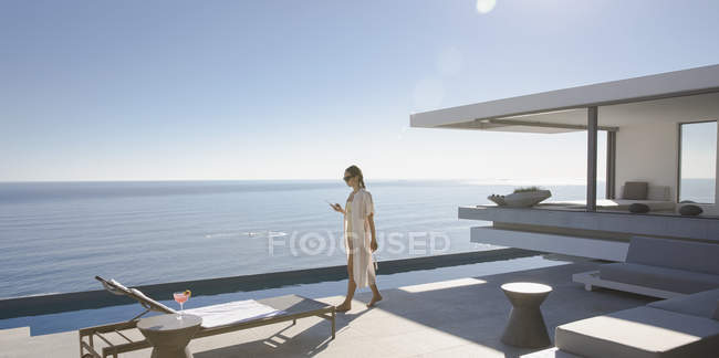 Женщина ходит по солнечной, современной, роскошный дом витрина внешний дворик с видом на океан — стоковое фото