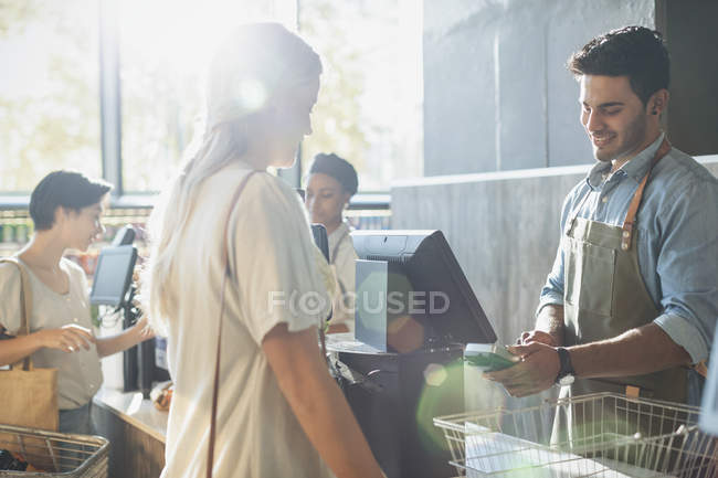 Male cashier helping female shopper at grocery store checkout — Stock Photo