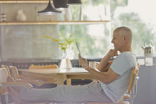Reifer Mann entspannt sich mit digitalem Tablet und Füßen am Esstisch — Stockfoto