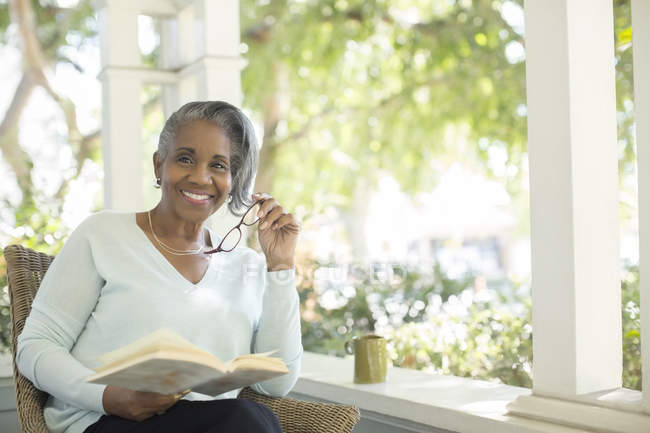Porträt einer lächelnden Seniorin, die Buch auf der Veranda liest — Stockfoto