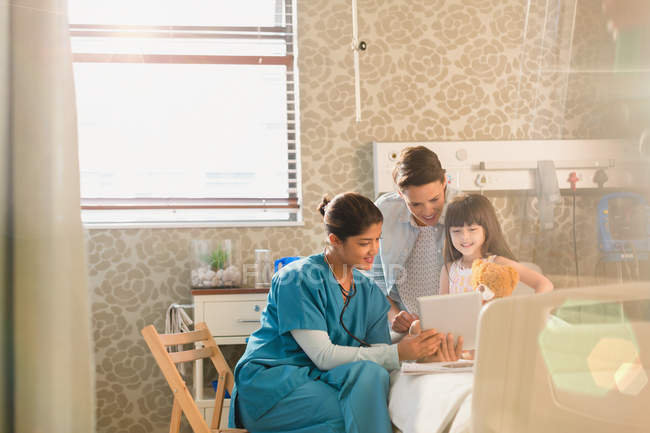 Женщина-медсестра показывает цифровые таблетки девочке и матери в больничной палате — стоковое фото