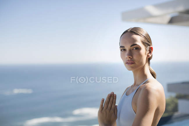 Portrait serene woman practicing yoga with hands at heart center on sunny patio with ocean view — Stock Photo