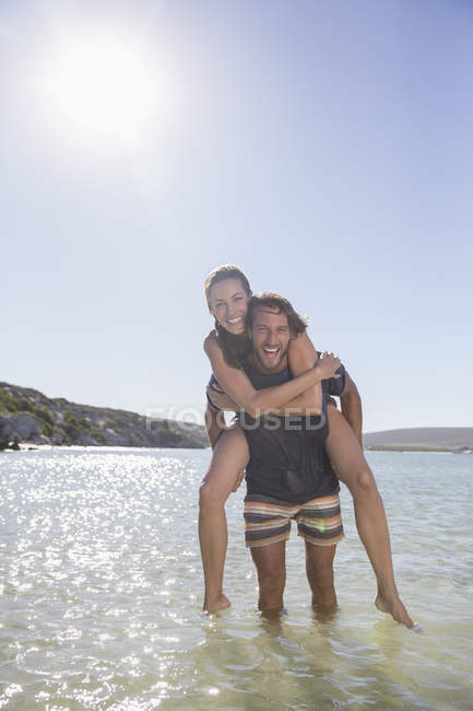 Woman being carried piggy back by boyfriend in waves — Stock Photo