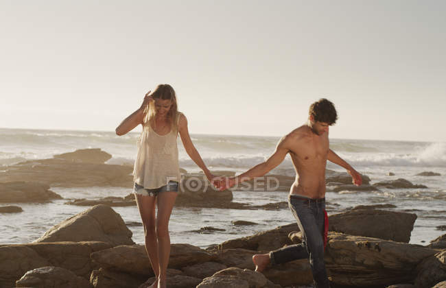 Young couple holding hands and walking on ocean rocks — Stock Photo