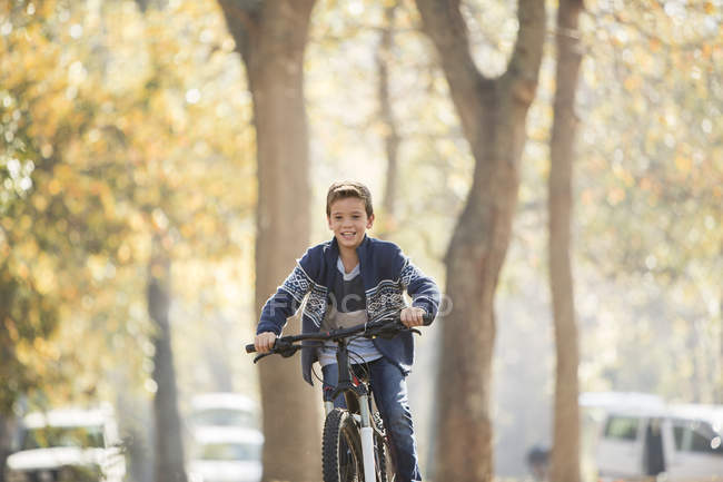 Chico sonriente montar en bicicleta en el parque - foto de stock