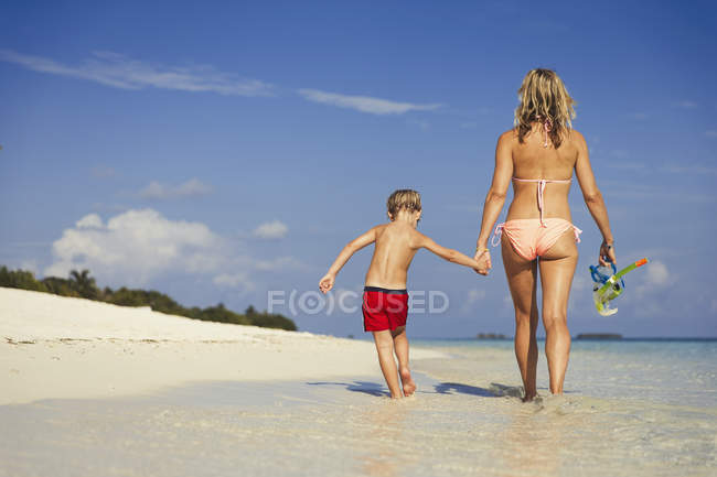 Mãe e filho caminhando na praia tropical ensolarada — Fotografia de Stock
