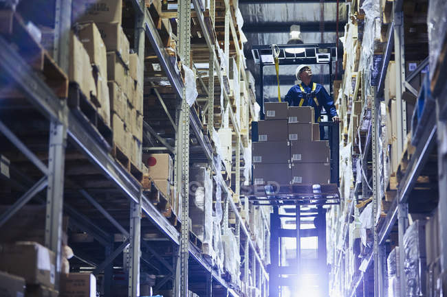 Рабочий штабелировщик вилочных погрузчиков укладывает картонные коробки на полки распределительного склада — стоковое фото