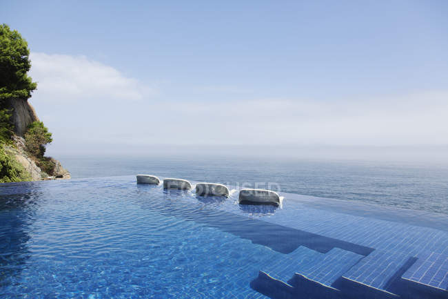 Крісла для відпочинку в нескінченному басейні з видом на океан — стокове фото