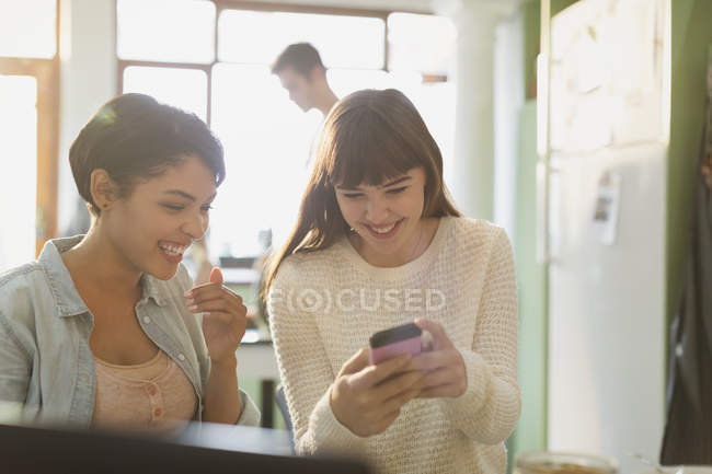 Smiling young women friends texting with cell phone — Stock Photo