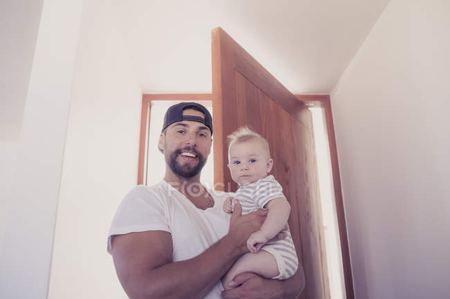 Portrait of smiling father holding baby son in doorway — Stock Photo