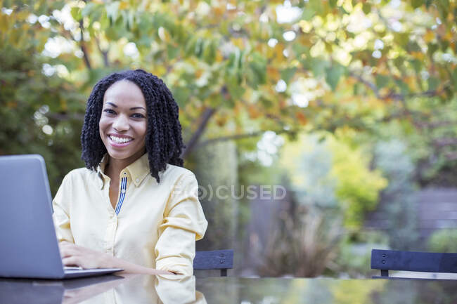 Портрет усміхається жінка, використовуючи ноутбук на патіо таблиці — стокове фото