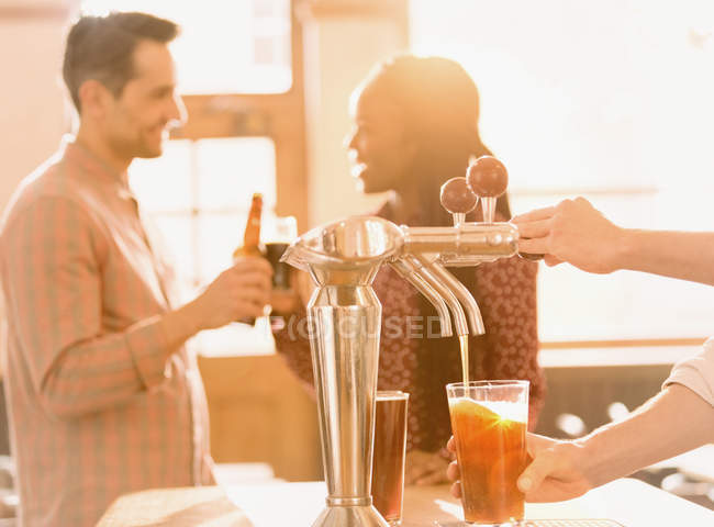 Couple drinking beer behind bartender pouring beer at beer tap in bar — Stock Photo