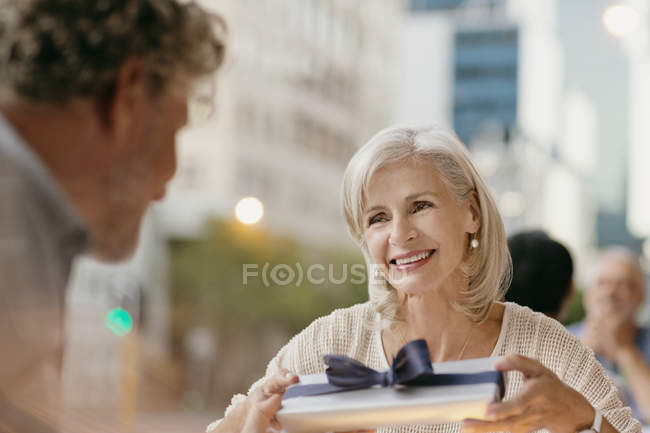 Senior woman receiving gift from husband at urban sidewalk cafe — Stock Photo