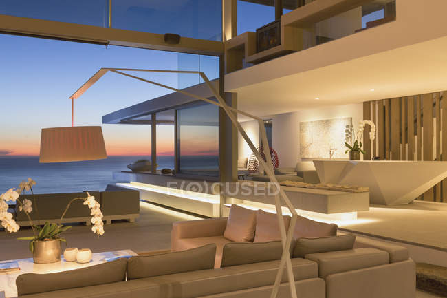 Illuminated, modern luxury home showcase interior living room with ocean view at dusk — Stock Photo