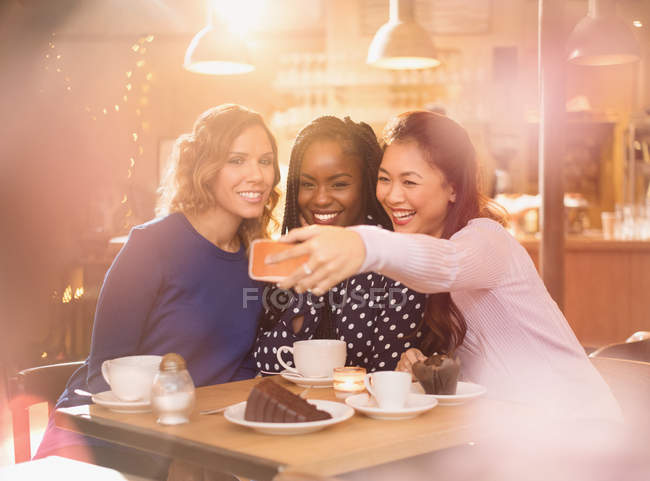 Smiling women friends taking selfie with camera phone at cafe table — Stock Photo