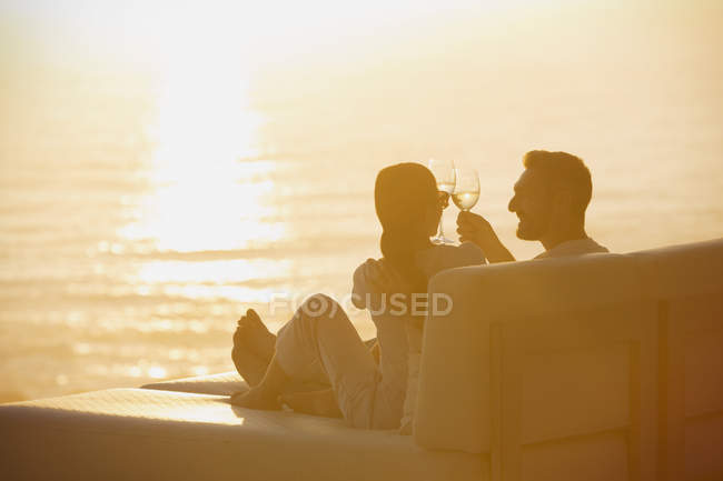 Силуетна пара тостів винних келихів на кріслі для відпочинку з видом на океан заходу сонця — стокове фото