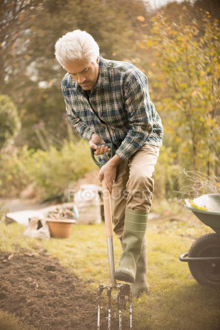 Jardinería del hombre cavando tierra en el jardín de otoño - foto de stock