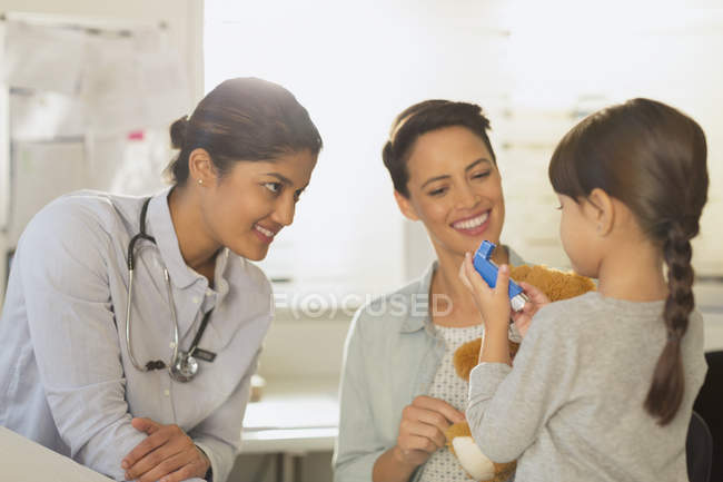 Pediatra e mãe assistindo menina paciente usando inalador na sala de exame — Fotografia de Stock
