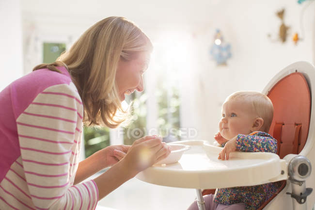 Madre alimentación bebé niña en silla alta - foto de stock