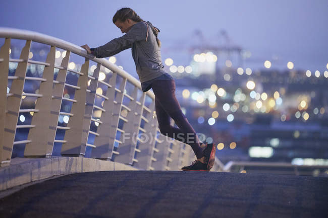 Female runner stretching legs on urban footbridge at dawn — Stock Photo