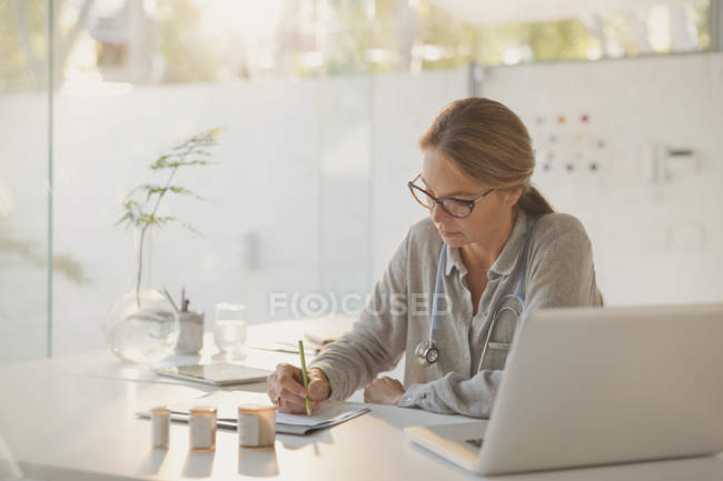 Female doctor writing prescriptions at desk in doctors office — Stock Photo