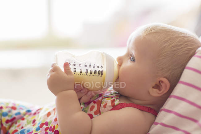 Bébé fille boire à partir de bouteille sur canapé — Photo de stock