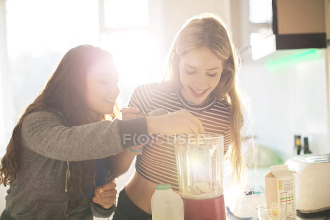 Adolescentes haciendo batido en la cocina soleada - foto de stock