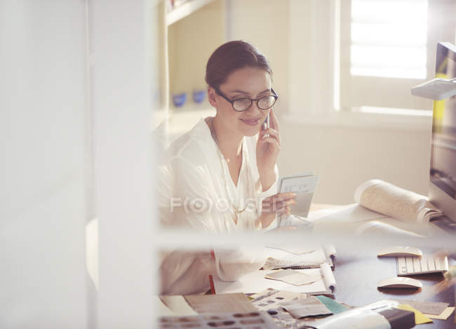 Interior designer examining fabric swatches and talking on cell phone in office — Stock Photo