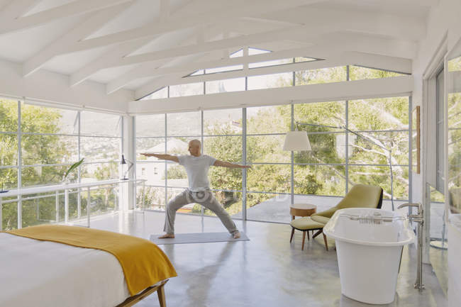 Älterer Mann praktiziert Yoga-Krieger 2 Pose in Luxus-Schlafzimmer — Stockfoto