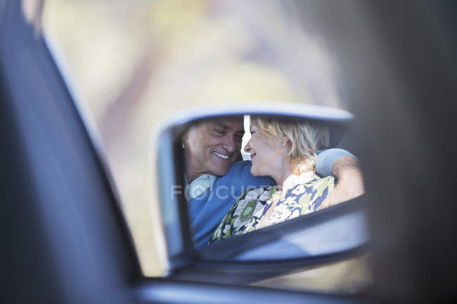 Side-view mirror reflection of couple hugging inside car — Stock Photo