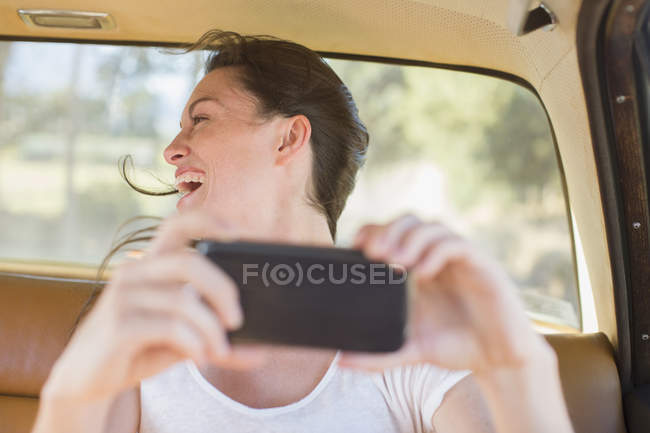 Femme dans le siège arrière de la voiture prenant des photos avec téléphone portable — Photo de stock