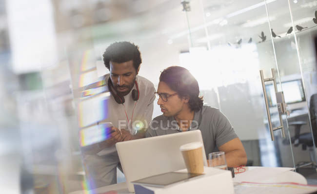 Des hommes d'affaires créatifs travaillant sur un ordinateur portable, utilisant un téléphone intelligent au bureau — Photo de stock